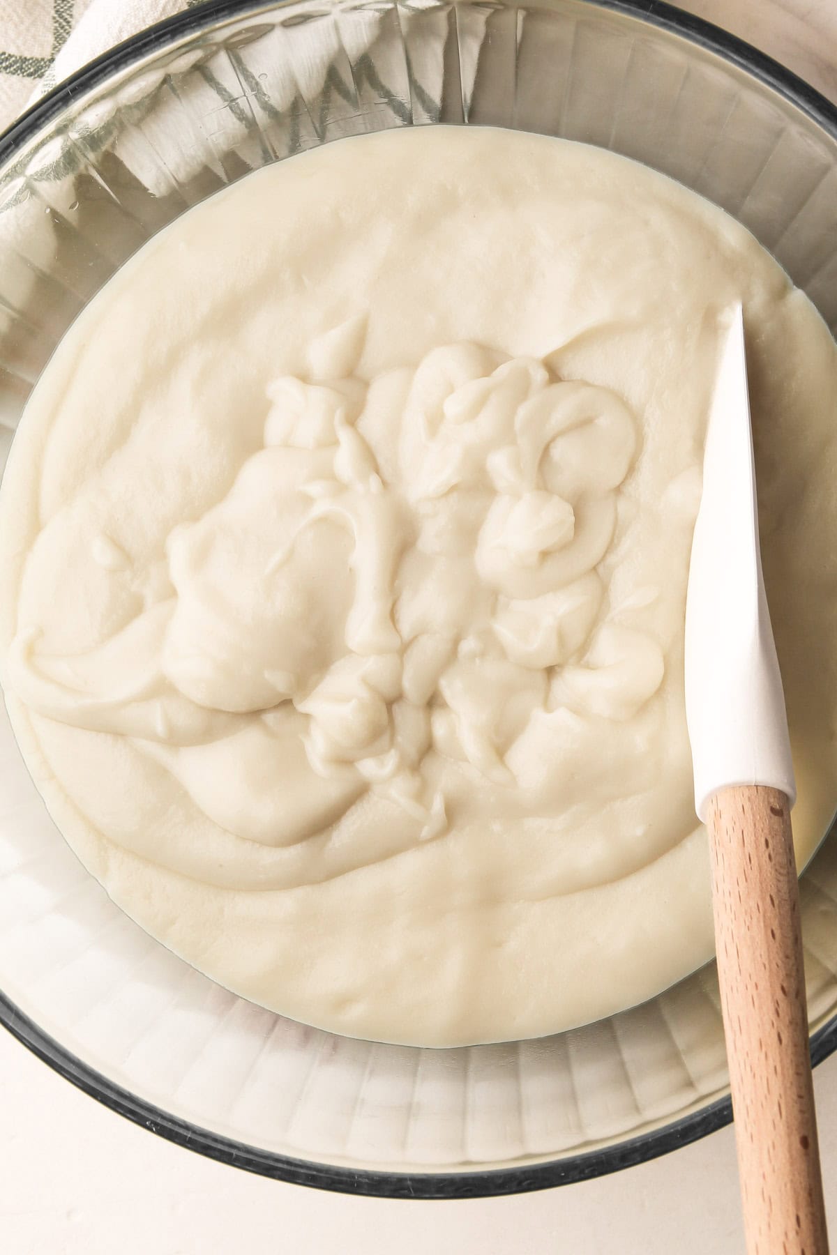 A bowl of strained coconut pudding made with coconut milk with a white spatula placed inside the bowl.