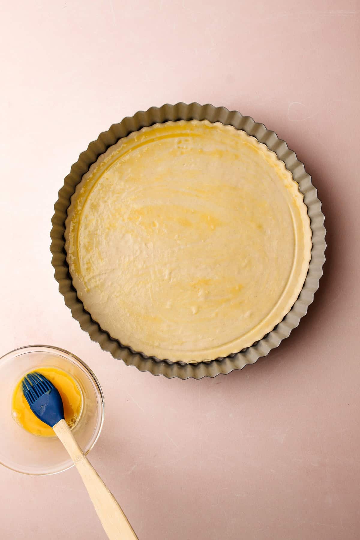 Puff pastry pressed into a tart pan being brushed with egg wash.