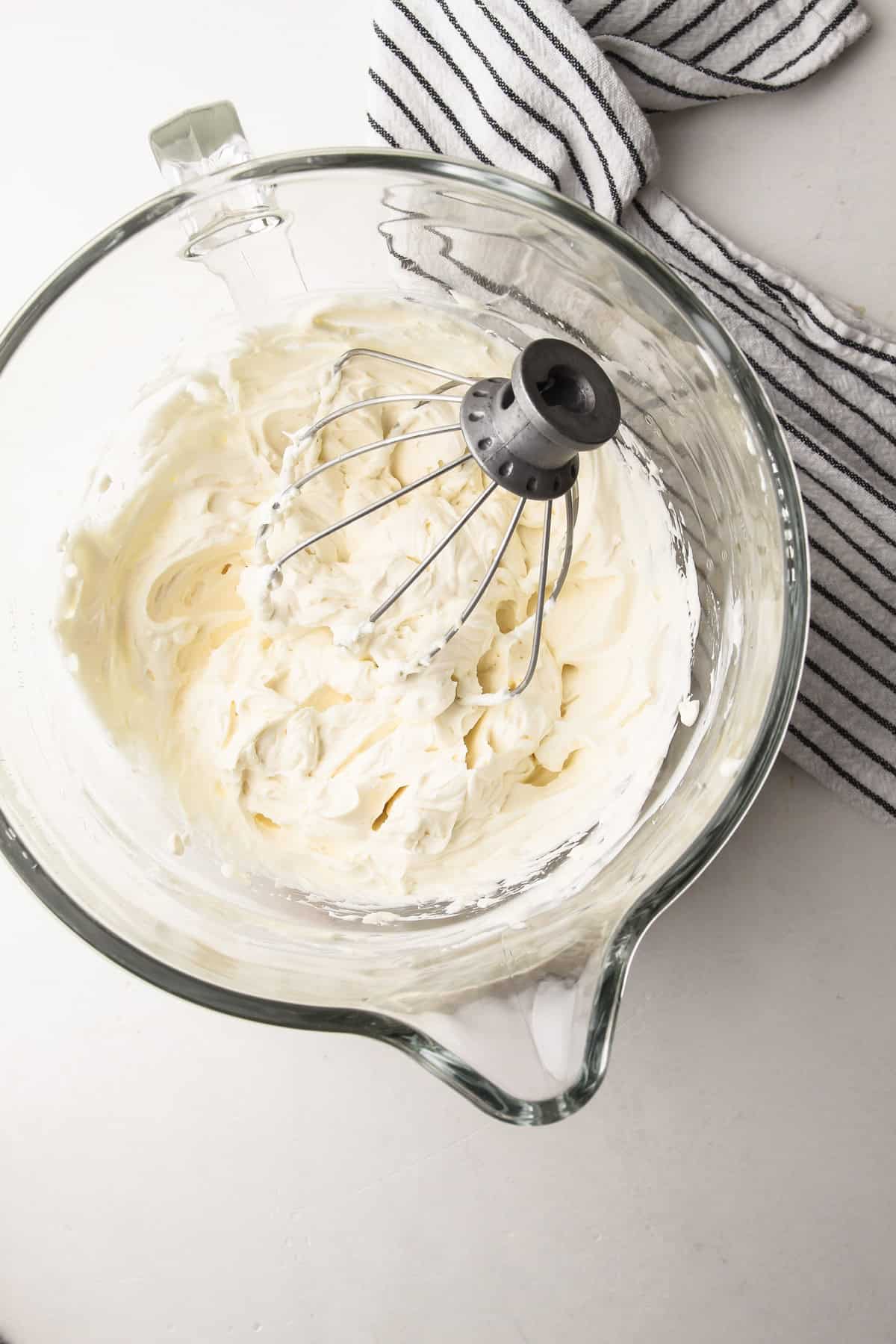 A glass stand mixer bowl with whipped cream cheese, vanilla extract and sugar in it for stabilized whipped cream.