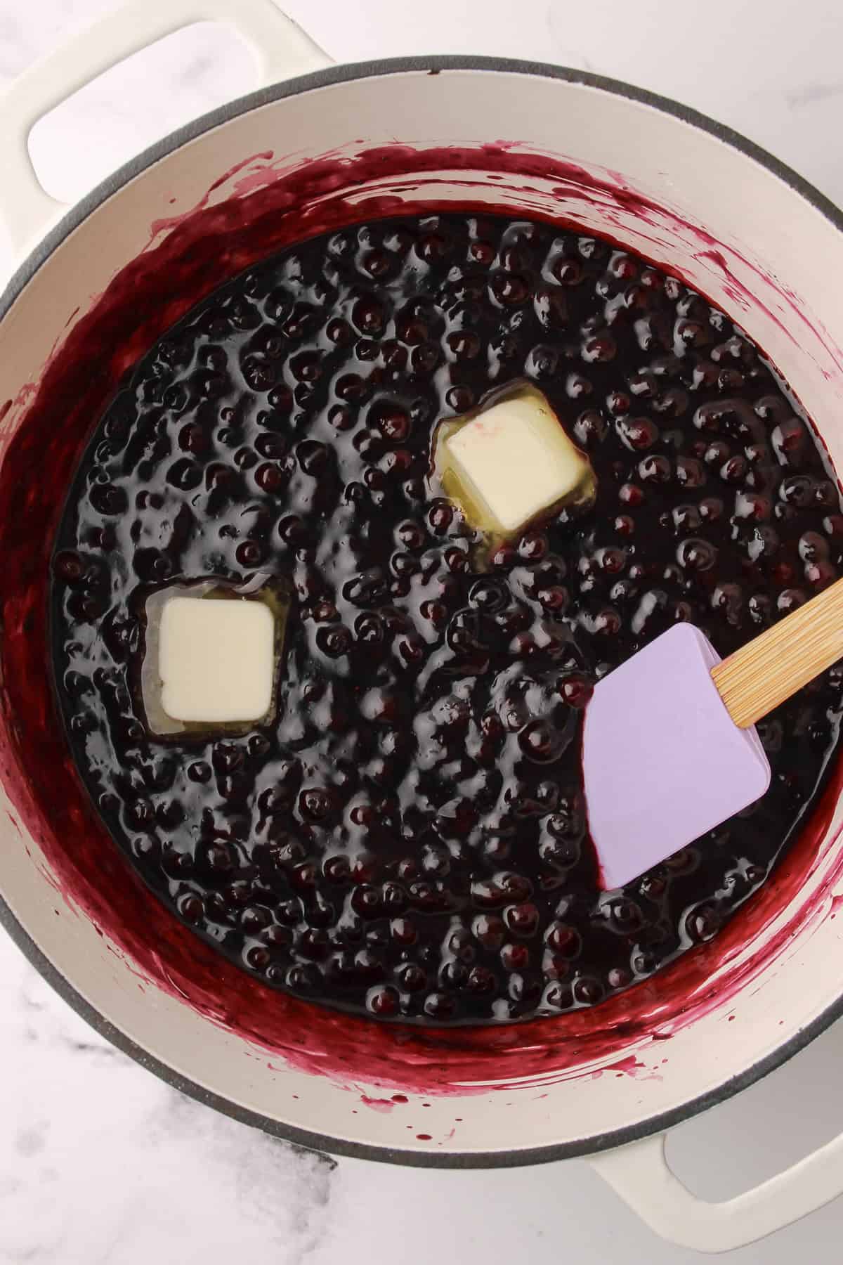 Cooked blueberry pie filling with two tablespoons of butter being swirled in.