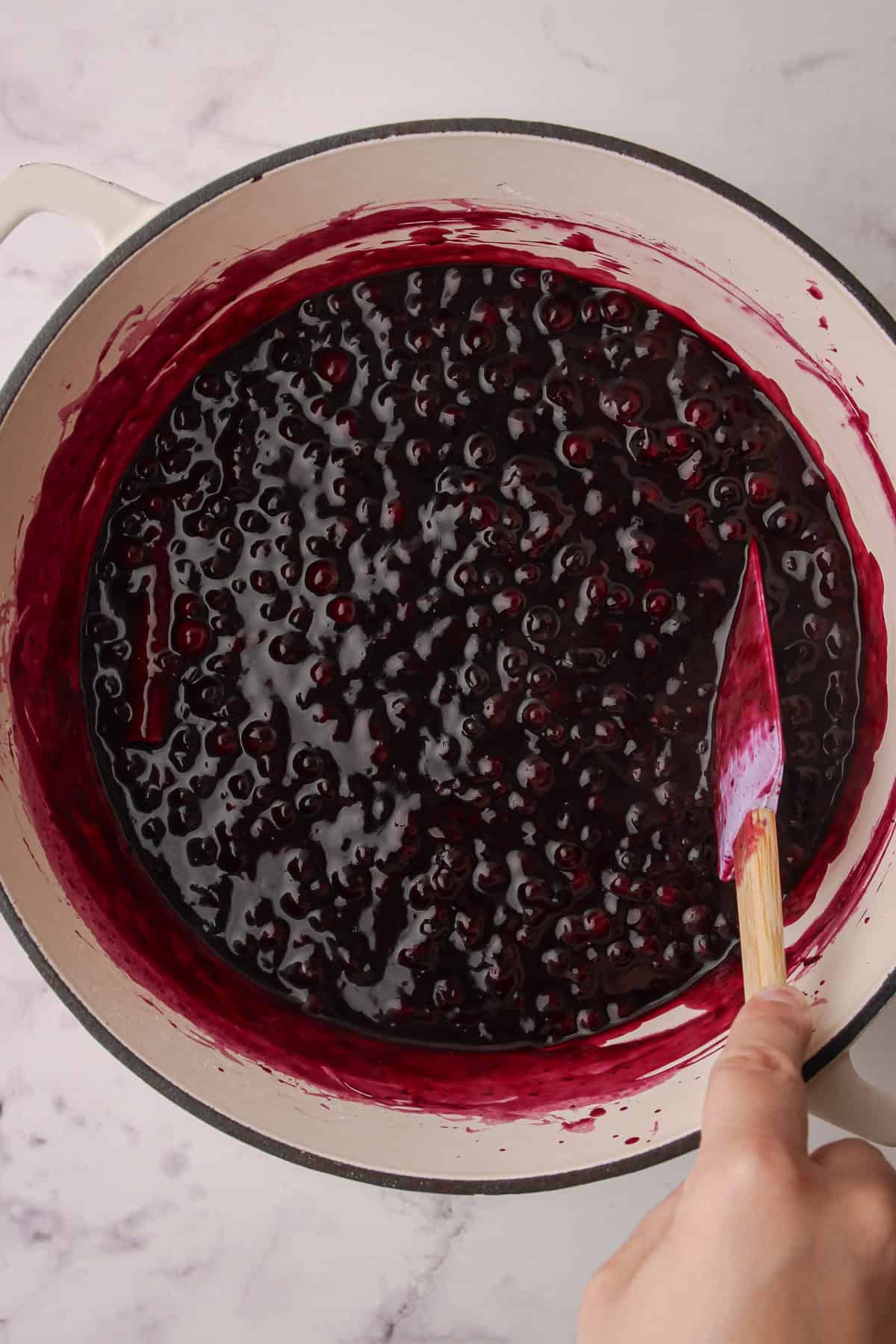Cooked blueberry pie filling in a white pot.