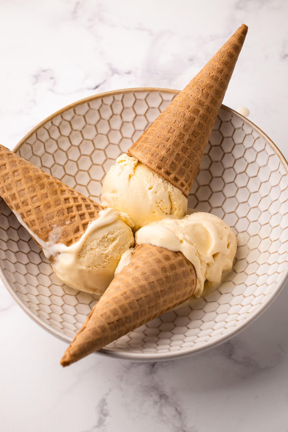 Three ice cream cones with homemade french vanilla ice cream inside of a bowl.