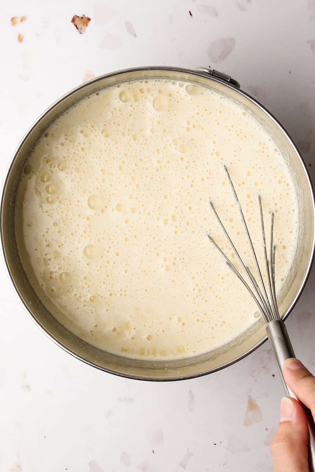 Egg yolks and sugar, milk and heavy cream being whisked together in a bowl for homemade french vanilla ice cream.