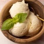 Three scoops of homemade basil ice cream in a wooden bowl with a sprig of fresh basil garnish.