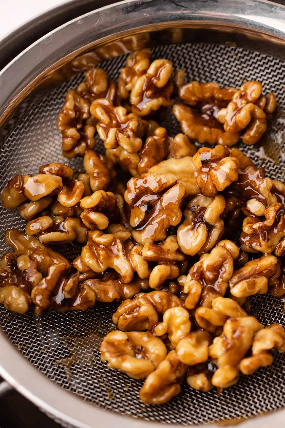 Maple syrup glazed walnuts sitting in a strainer.