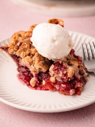 A slice of nectarine plum pie with a jammy filling topped with ice cream.