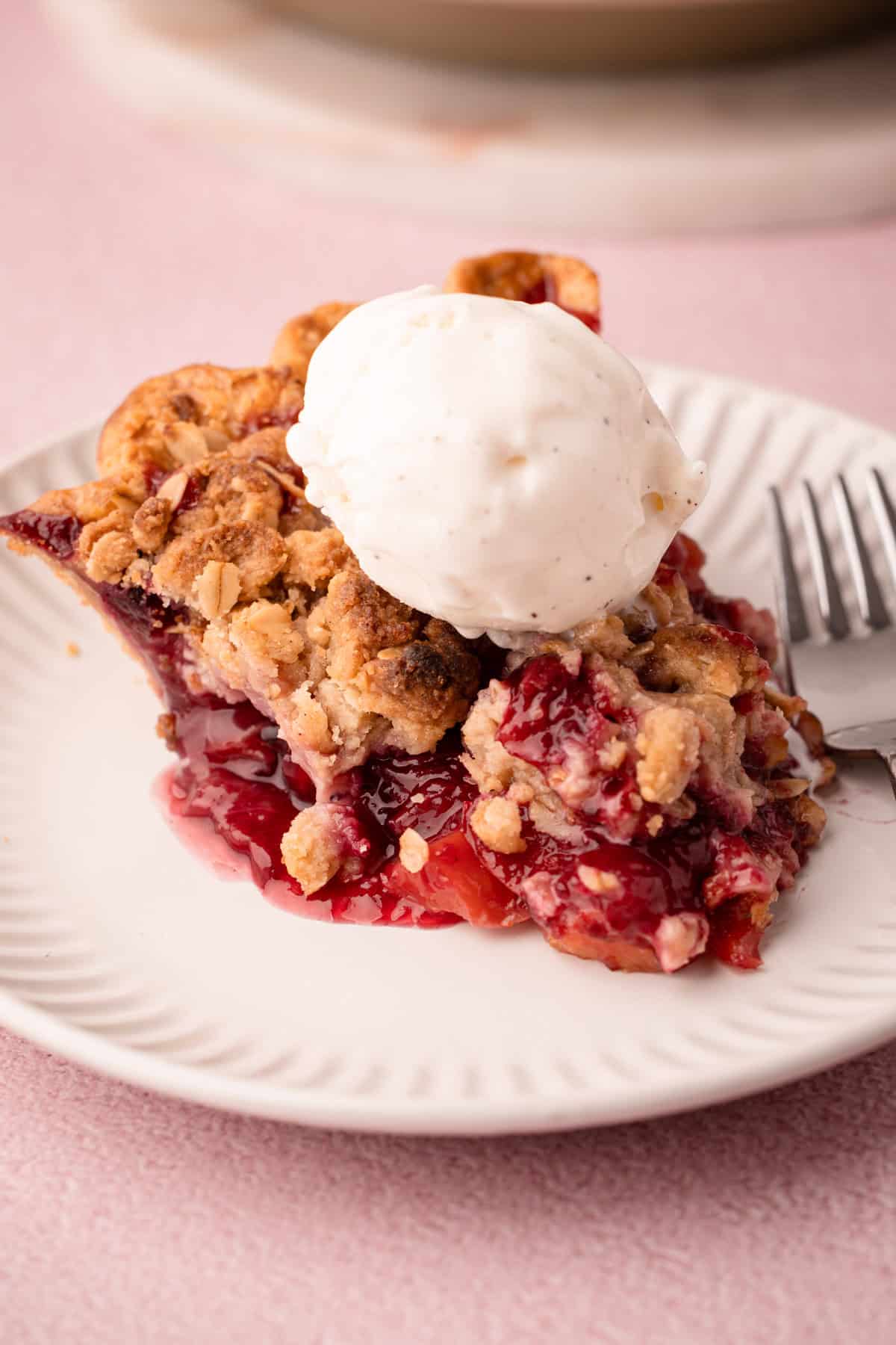 A slice of nectarine plum pie with a jammy filling topped with ice cream.