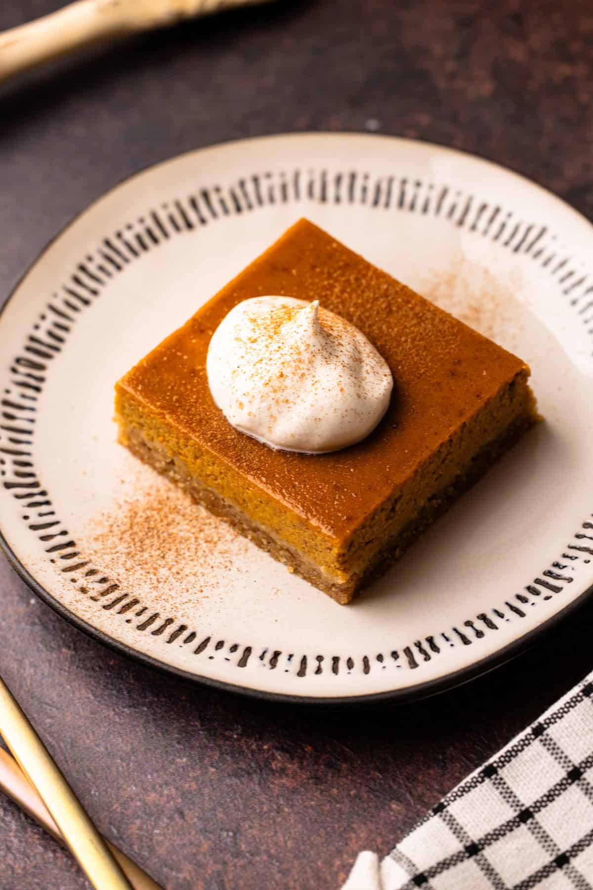 A serving of a pumpkin pie bar with whipped cream and a sprinkle of cinnamon.