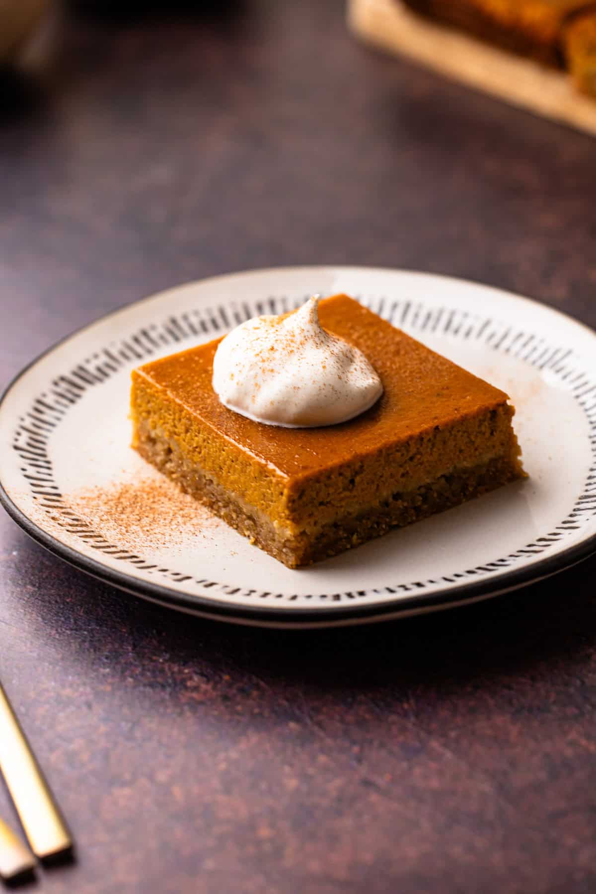 A serving of a pumpkin pie bar with whipped cream and a sprinkle of cinnamon.