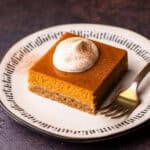 A serving of a pumpkin pie bar with whipped cream and a sprinkle of cinnamon.