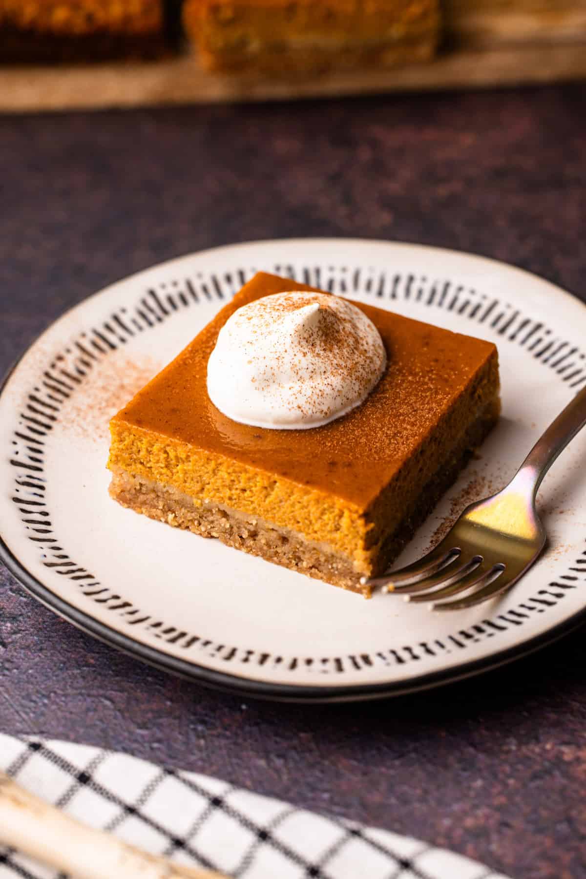 A serving of a pumpkin pie bar with whipped cream and a sprinkle of cinnamon.