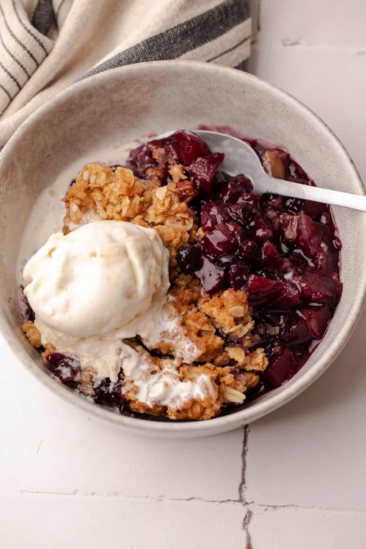 A serving of baked apple blueberry crisp with a scoop of ice cream in a bowl.