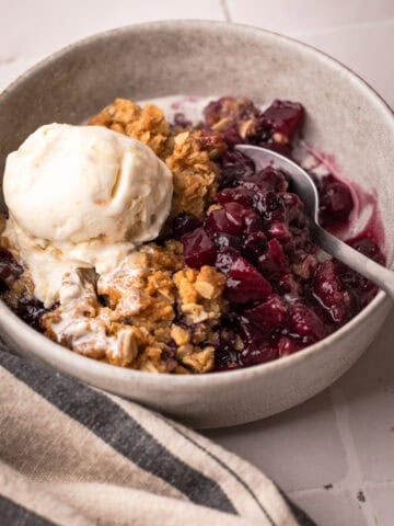 A serving of baked apple blueberry crisp with a scoop of ice cream in a bowl.