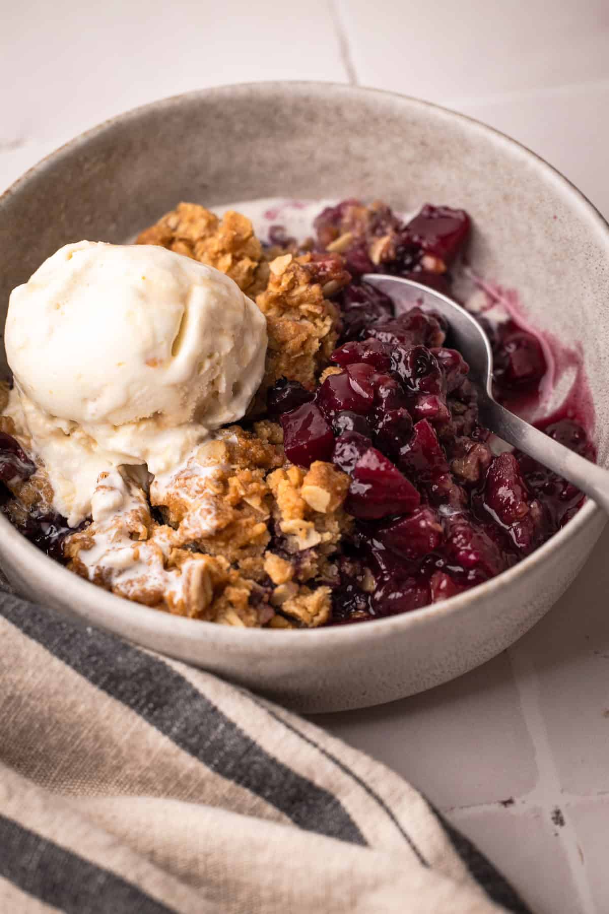 A serving of baked apple blueberry crisp with a scoop of ice cream in a bowl.