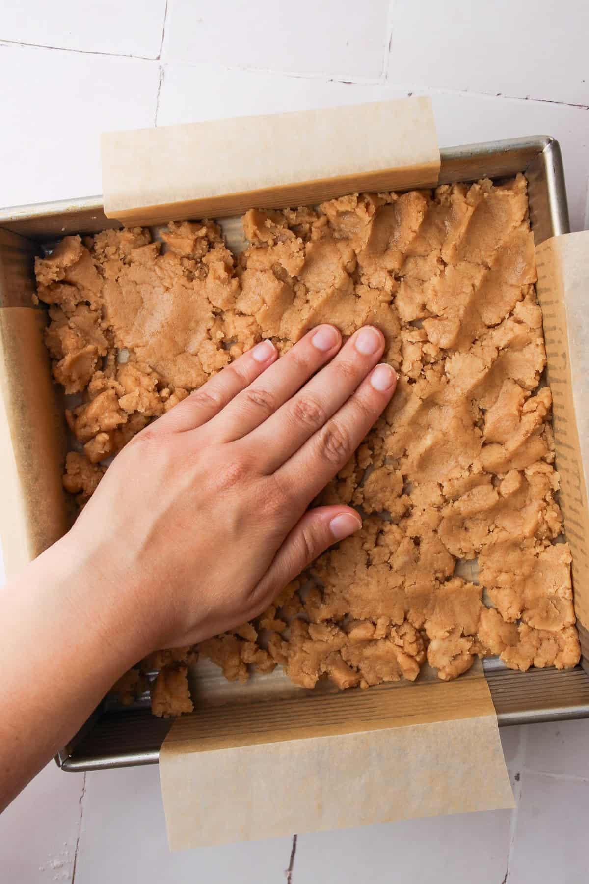 Patting down the crumbled shortbread in a square pan.