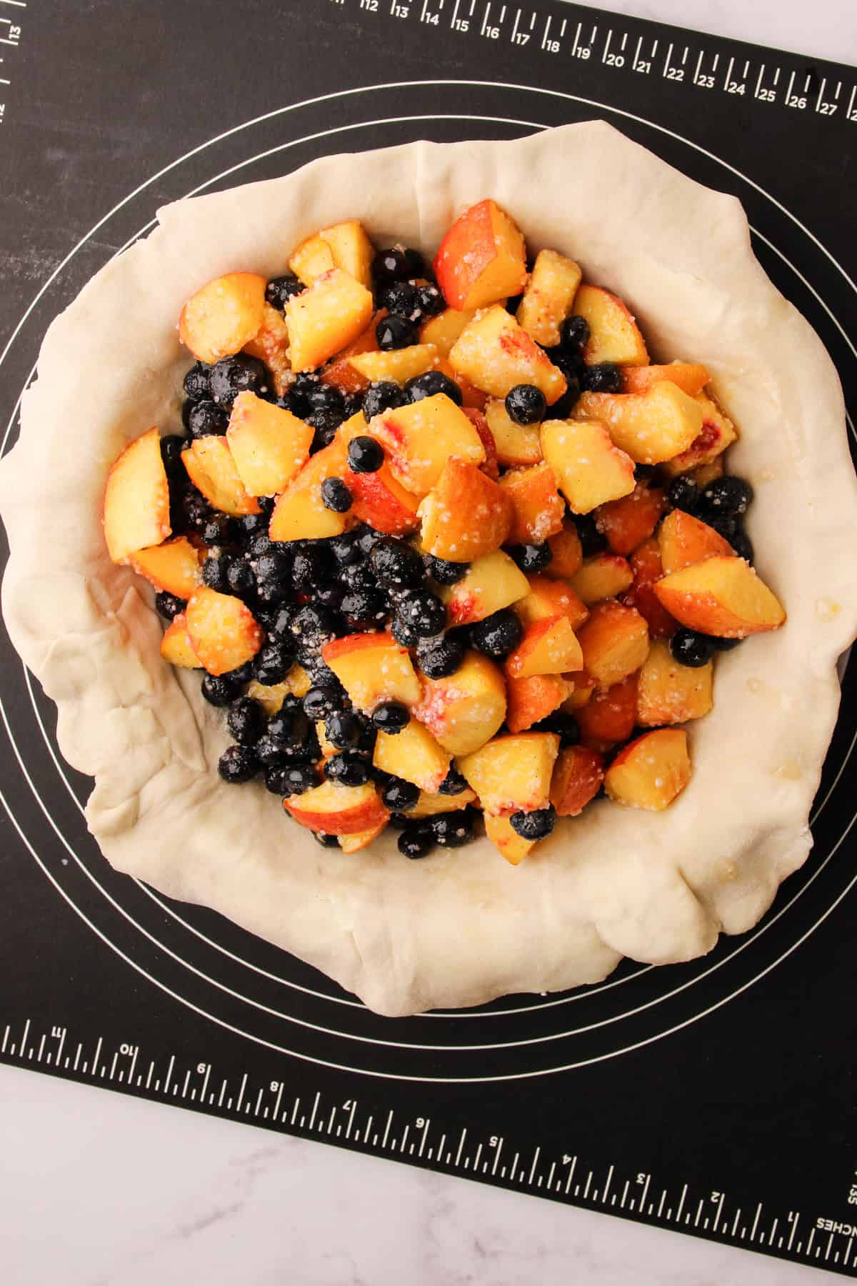 Unbaked peach blueberry pie filling inside of pie dough being assembled.