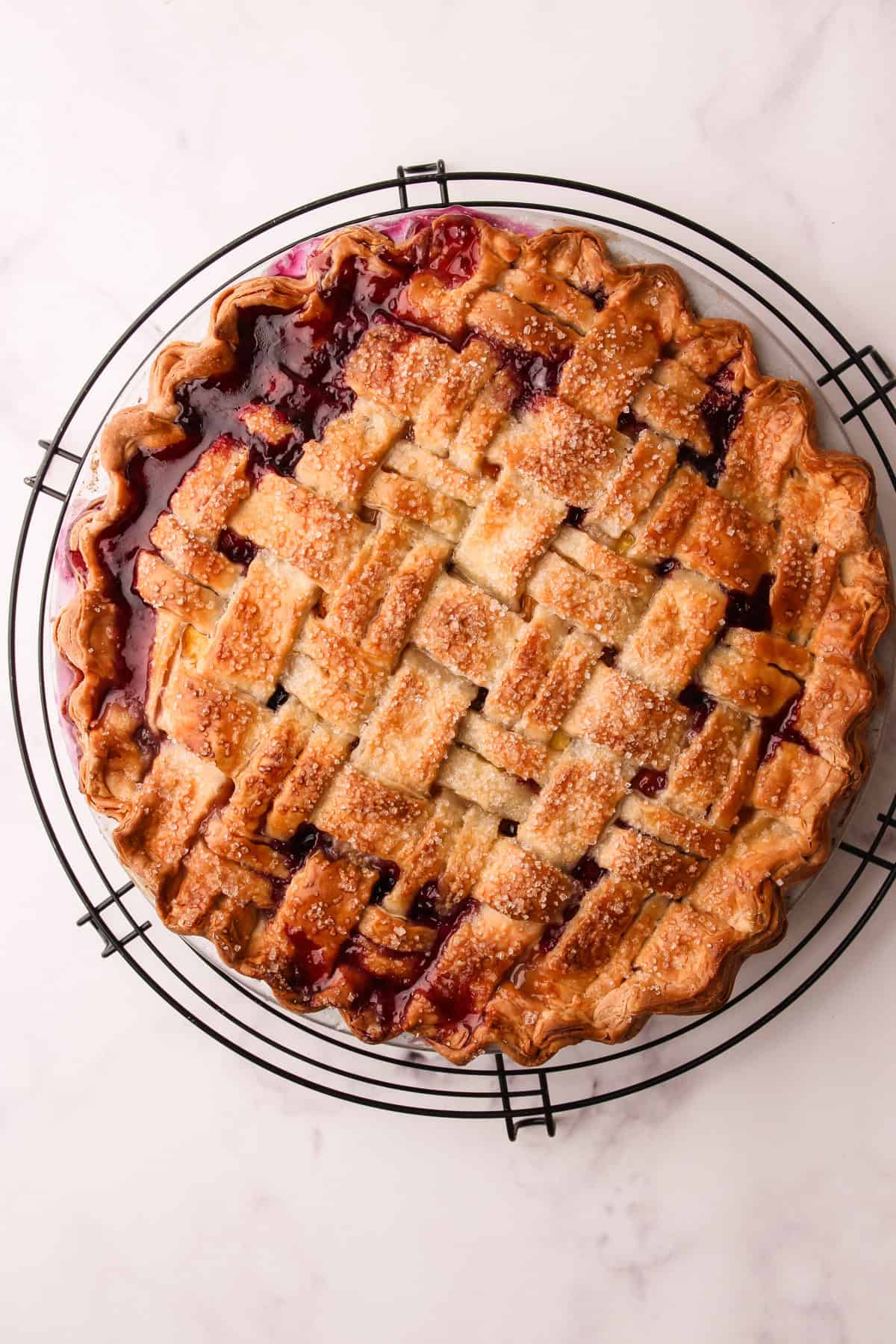 A baked blueberry peach pie on a cooling rack.