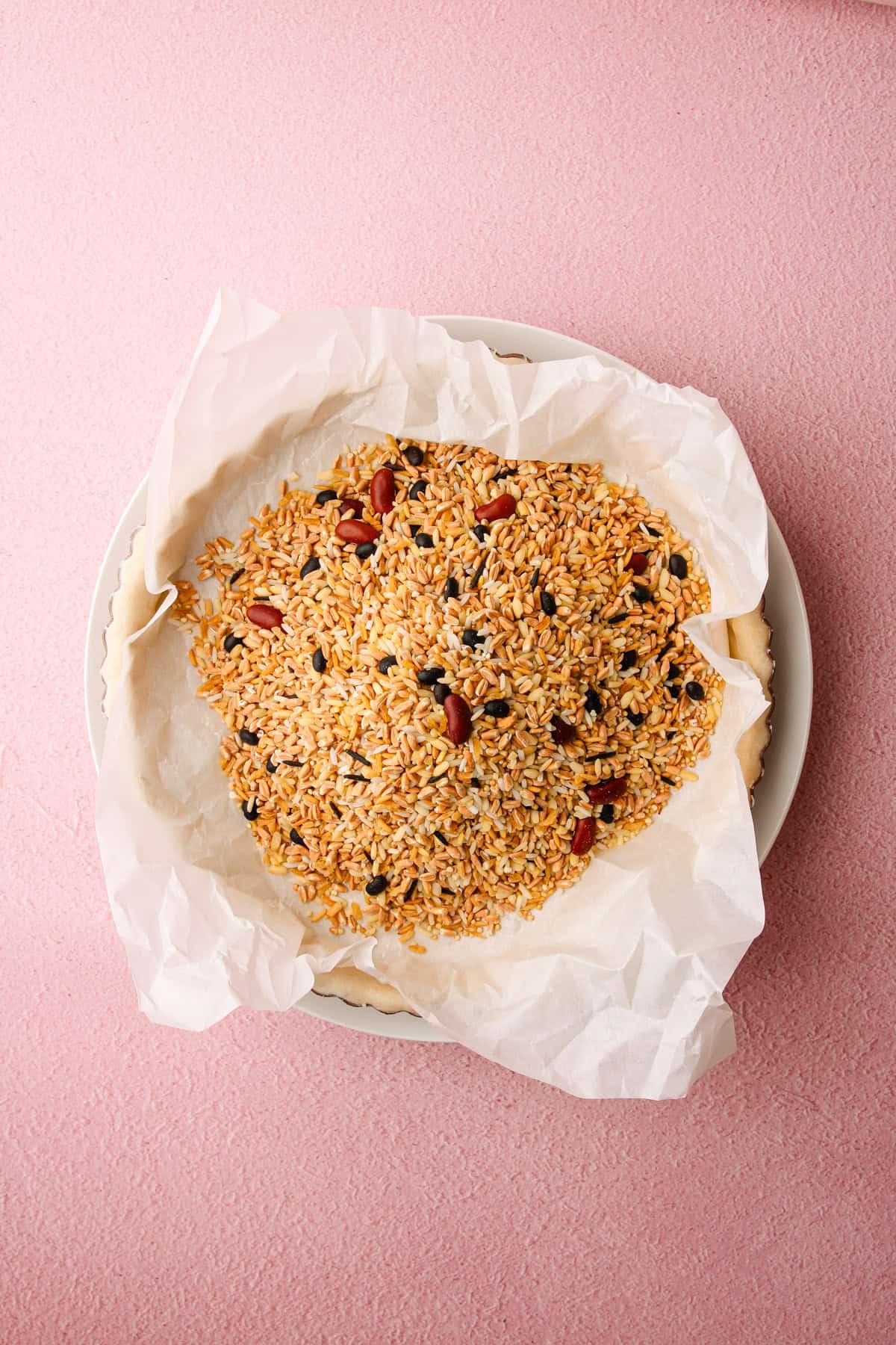An unbaked tart crust with parchment paper and dried beans weighing it down before baking.