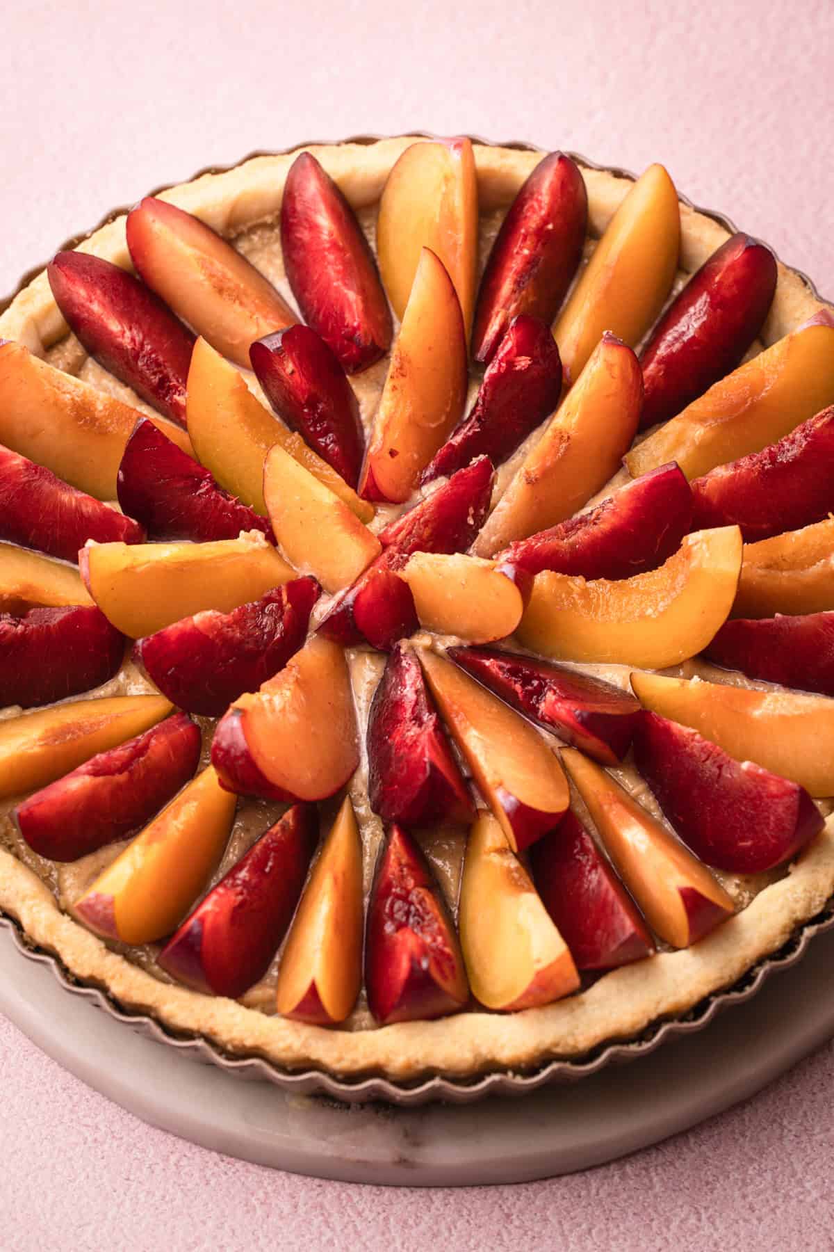 An assembled but unbaked plum tart with alternative colors of plums.