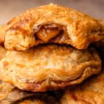 Baked apple hand pies, stacked on top of each other with a bite revealing the apple pie filling inside.