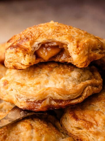 Baked apple hand pies, stacked on top of each other with a bite revealing the apple pie filling inside.