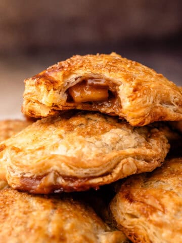 Baked apple hand pies, stacked on top of each other with a bite revealing the apple pie filling inside.