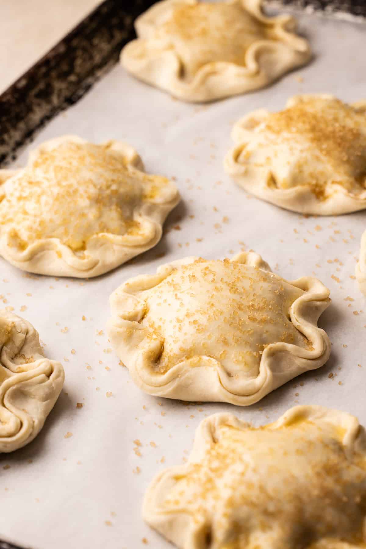 Apple hand pies assembled and unbaked on a sheetpan.