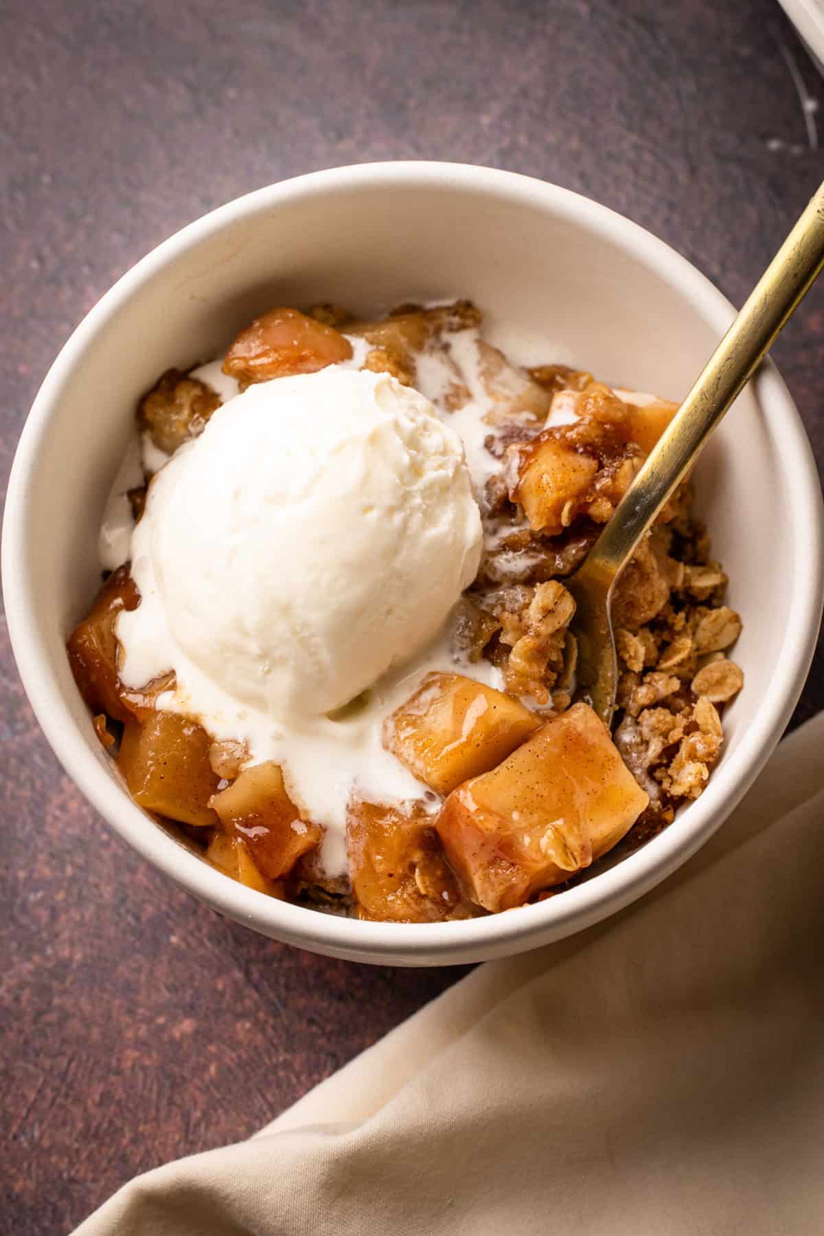 A bowl of pear apple crisp with a scoop of ice cream on top.