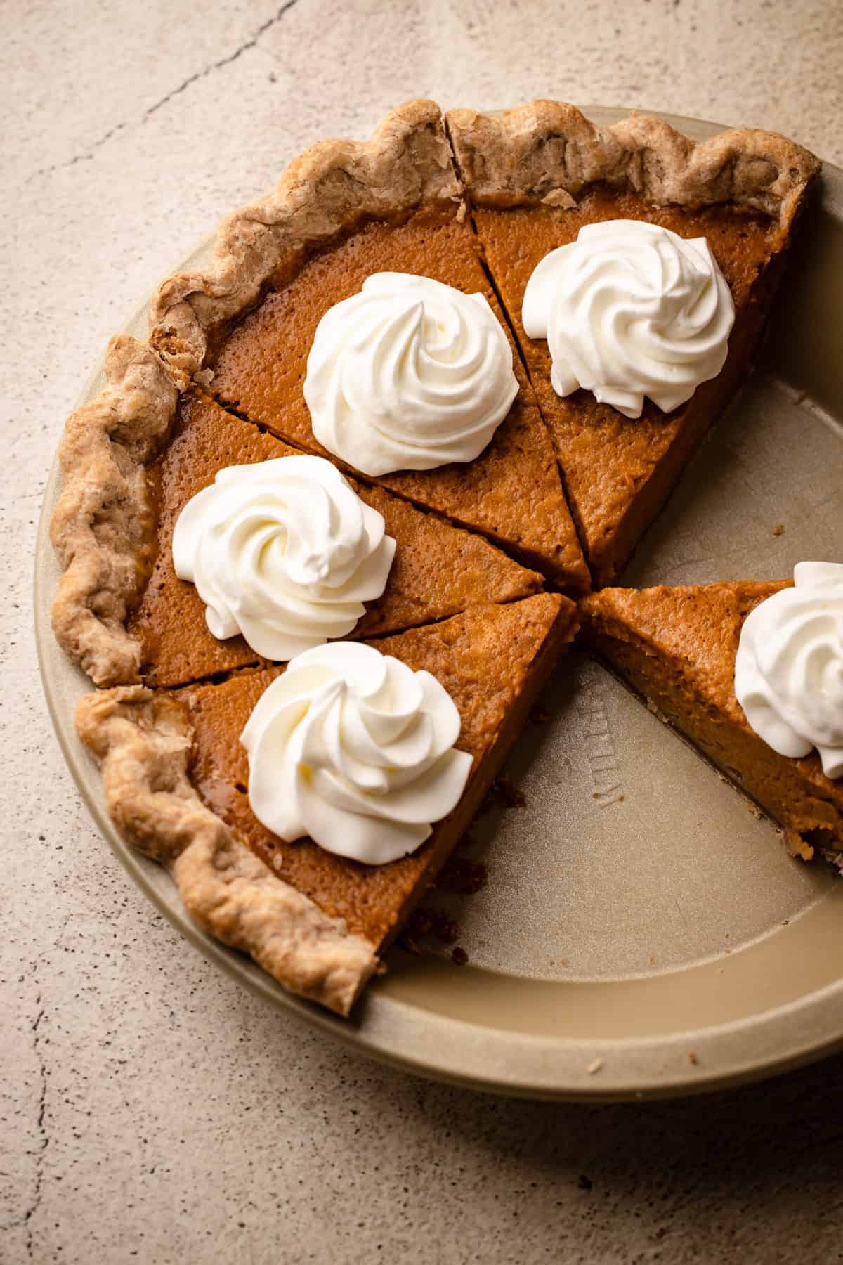 A pumpkin pie baked, cooled and sliced with homemade whipped cream.