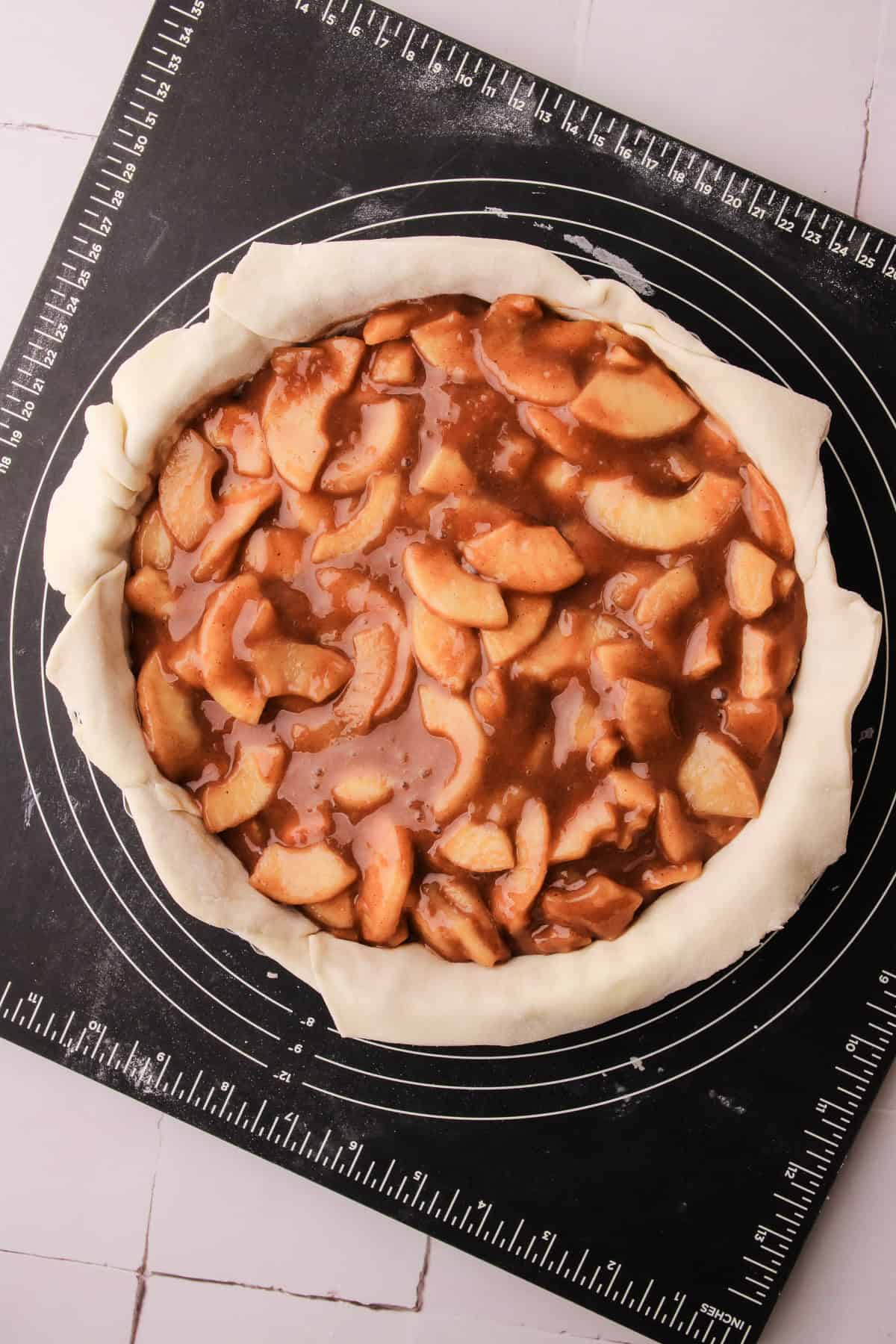 A puff pastry lined tart pan filled with precooked filling to make an apple pie.