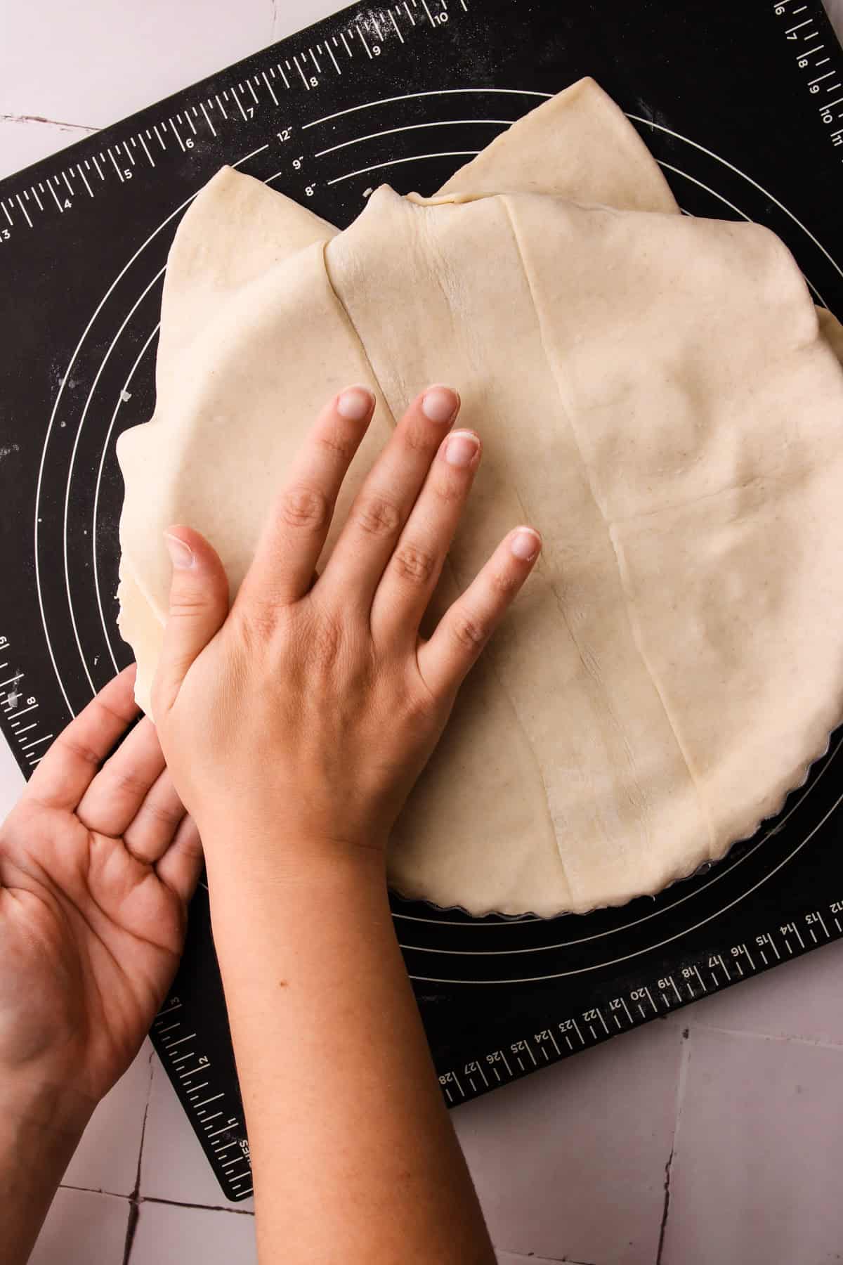 Placing the top of the puff pastry on an unbaked apple pie.