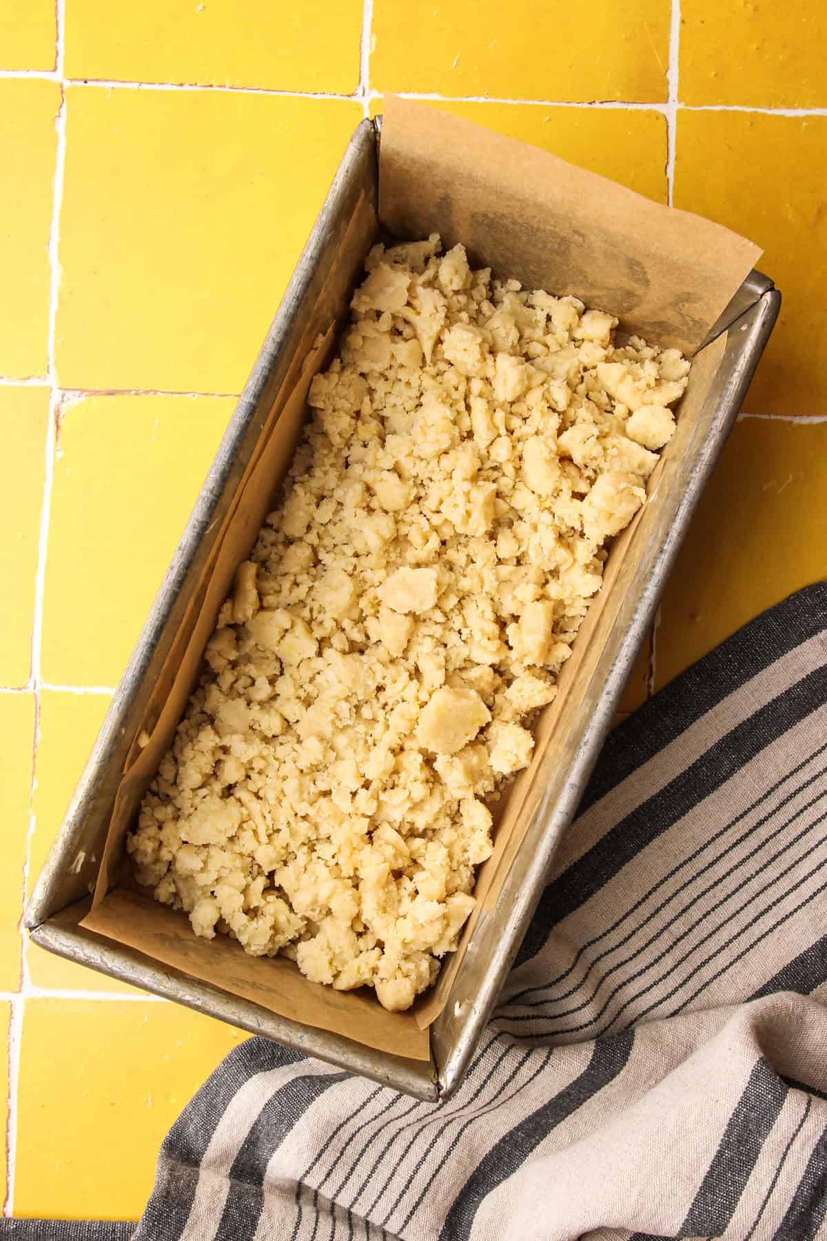 The crumbled shortbread spread evenly in a loaf pan for lemon pie bars.