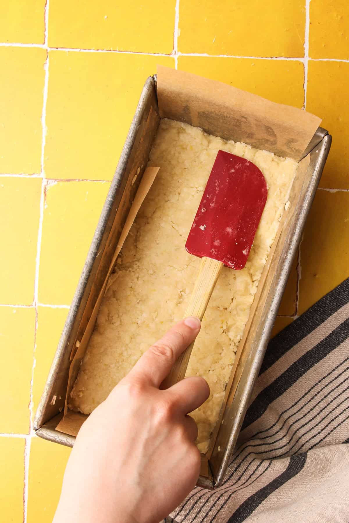 Pressing crumbled shortbread layer evenly in a loaf pan for lemon pie bars.