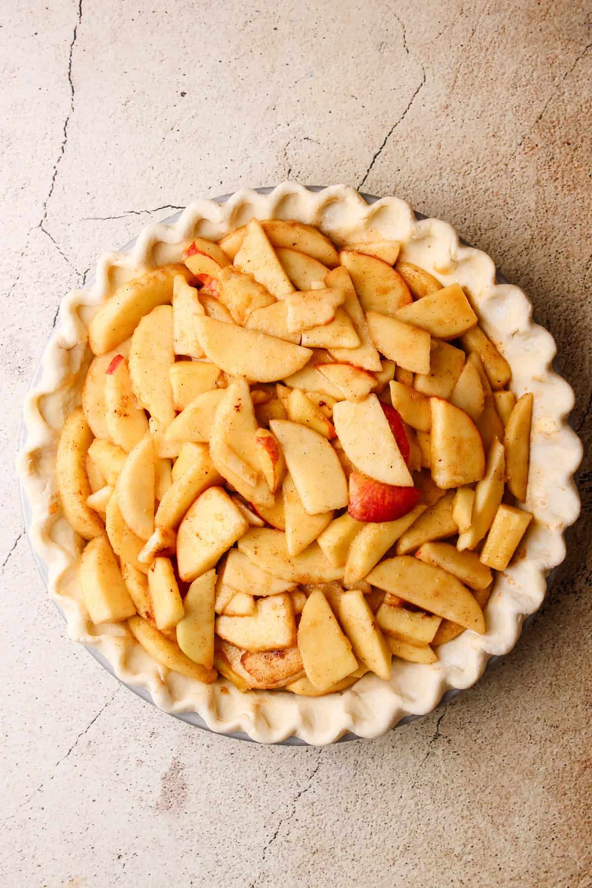 Apple slices being layered into an unbaked pie crust.