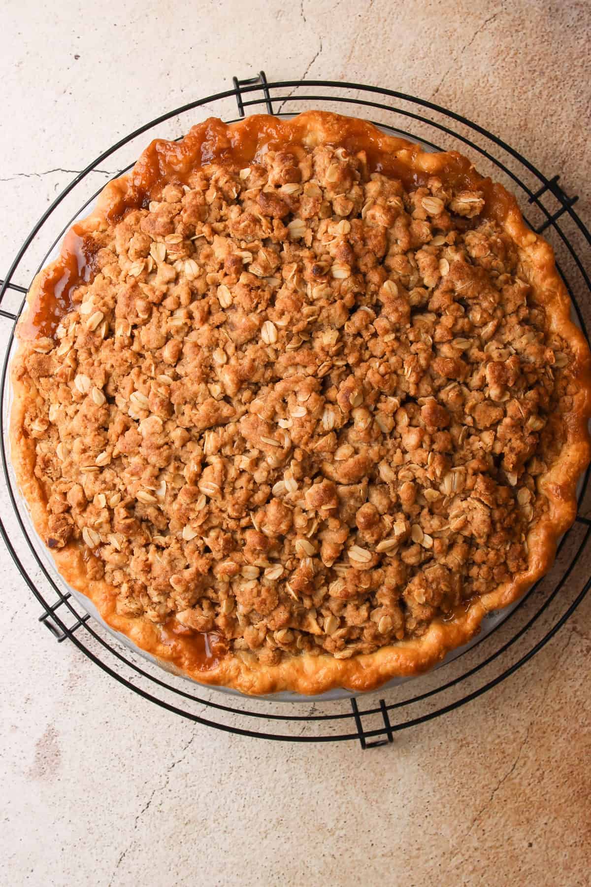 A whole baked apple pie with a crumb topping cooling on a wire rack.