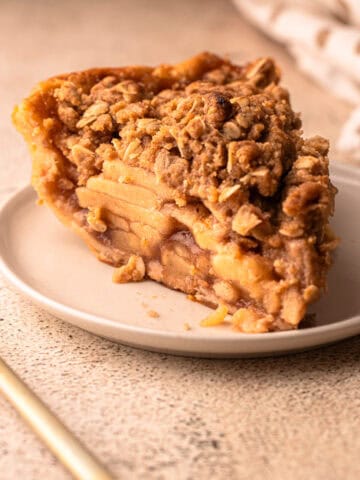 A close-up of a slice of apple crumb pie with a golden oat topping.